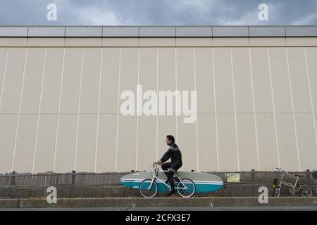 Ein Surfer fährt mit einem Pushbike mit einem Surfbrett auf einem Gehweg entlang des Enoshima Beach, Kanagawa, Japan. Stockfoto