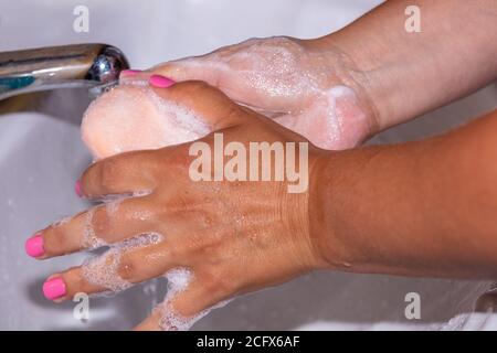 Nahaufnahme einer Frau, die ihre Hände mit einem Seifenstück mit Leitungswasser faulte. Rosa Fingernägel. Hygienekonzept. Stockfoto