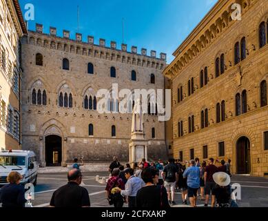 Toller Blick auf die beliebte Piazza Salimbeni in Siena, Toskana, Italien. Touristen schauen sich die Statue der lokalen religiösen Figur Sallustio... Stockfoto