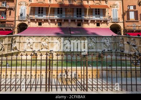 Schöner Blick auf den monumentalen Brunnen Fonte Gaia auf der Piazza del Campo von Siena, Italien. Das rechteckige Becken ist von einem eisernen Zaun... Stockfoto