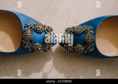 Draufsicht auf den Verlobungsring der Braut mit einem Edelstein zwischen blauen Schuhen mit Schmuckdeko. Stockfoto