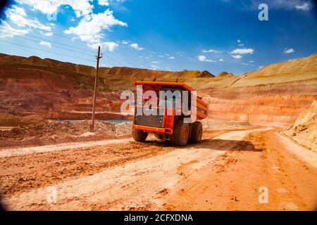 Orange Hitachi Steinbruch Muldenkipper mit Bauxit. Aluminiumerz Bergbau und Transport. Tagebau. Steinbruch. Am blauen Himmel mit weißen Wolken. Stockfoto