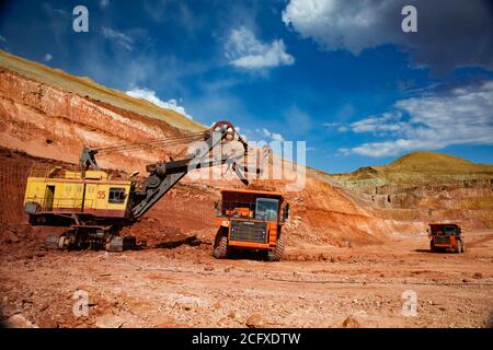 Aluminiumerz Bergbau und Transport. Bauxit Tonerde Tagebau (Steinbruch). Gelbe Bagger beladen orange Hitachi Steinbruch LKW (Kipper). Stockfoto