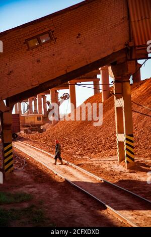 Aluminiumerz Bergbau und Transport. Bauxit Lehm Ladetrichter Auto Zug Terminal. Bagger mit Gelände Haufen und Arbeiter in roten Helm. Stockfoto