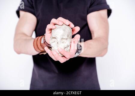 Ein Mann in einem schwarzen T-Shirt und mit Lederarmbändern An seinen Händen hält ein menschlicher Schädel Stockfoto