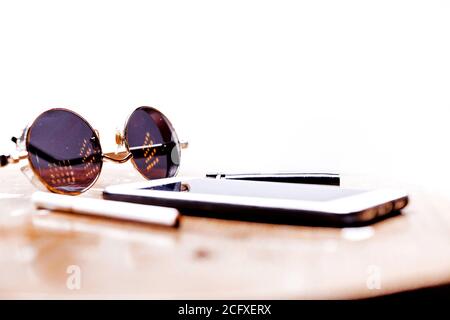 Zigaretten, Sonnenbrille, Brille und Telefon liegen auf einem Holztisch auf weißem Hintergrund. Brutaler Mann Stockfoto