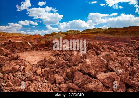 Aluminiumerz-Steinbruch. Bauxit-Tonerde-Tagebau. Steinbruchsteine. Haufen leerer Steine mit grünem Gras. Blauer Himmel mit Wolken. Stockfoto