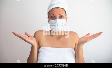 Frau mit medizinischer Maske und Kopf und Körper in frischen weißen Handtüchern in einem Spa vor weißem Hintergrund gewickelt. Eine Frau in einem Spa während einer Coronapandemie Stockfoto