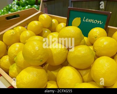 Künstliche gelbe Zitronen in einer Holzkiste als Marktdesign auf dem Hintergrund anderer Gemüse und Früchte, weicher Fokus. Stockfoto