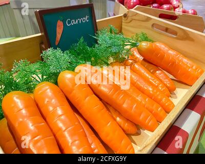 Künstliche orange Karotten in einer Holzkiste als Marktdesign auf dem Hintergrund von anderen Gemüse und Obst, weichen Fokus. Stockfoto