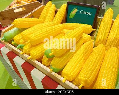 Künstliche gelbe Hühneraugen in einer Holzkiste als Marktdesign auf dem Hintergrund anderer Gemüse und Früchte, weicher Fokus. Stockfoto