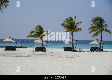 Eine Reihe schattiger Sonnenliegen und Palmen säumen den Strand eines Luxusresort auf den Malediven. Stockfoto