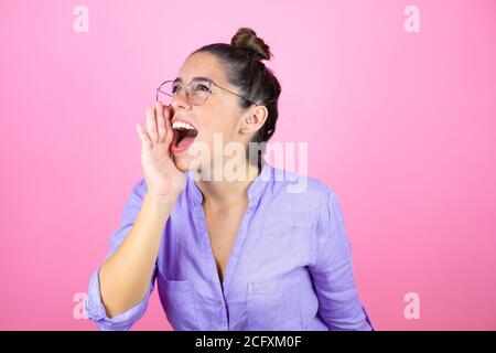 Junge schöne Frau trägt Brille über isoliert rosa Hintergrund schreien Und schreiend laut zur Seite mit der Hand auf dem Mund Stockfoto