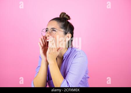Junge schöne Frau trägt Brille über isoliert rosa Hintergrund schreien Und schreiend laut zur Seite mit den Händen auf dem Mund Stockfoto