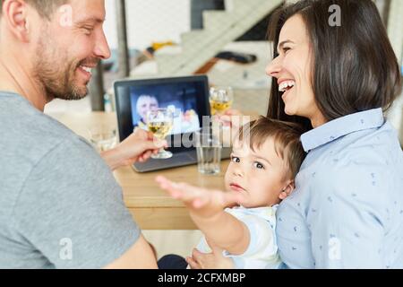 Glückliches Paar mit Kind trinkt Wein im Video-Chat online Auf einem Laptop-Computer Stockfoto