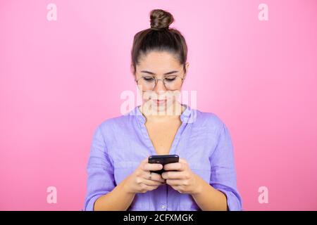 Junge schöne Frau trägt Brille über isoliert rosa Hintergrund Texting Mit ihrem Telefon Stockfoto