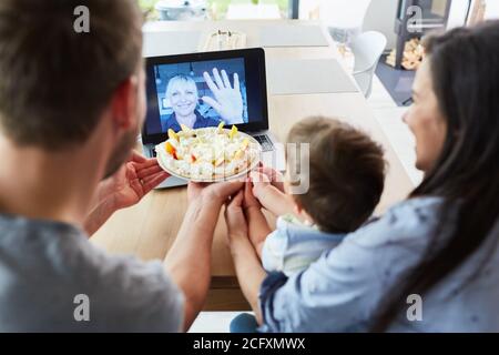 Familie mit Kind im Videochat mit Großmutter am Geburtstag Hausgemachter Kuchen Stockfoto