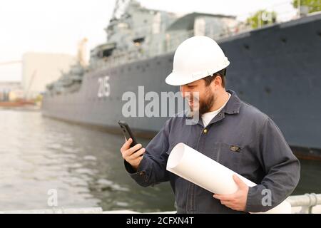 Marine glücklich Ingenieur im Gespräch mit VHF Walkie Talkie, hält Papiere in der Nähe des Schiffes im Hintergrund. Stockfoto