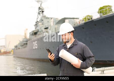 Marineingenieur im Gespräch mit VHF-Walkie-Talkie, hält Papiere in der Nähe des Schiffes im Hintergrund. Stockfoto