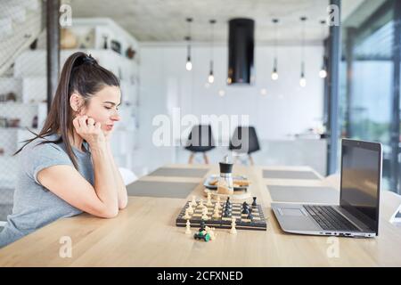 Frau zu Hause spielen Schach auf Laptop-Computer denken über Video-Chat online Stockfoto