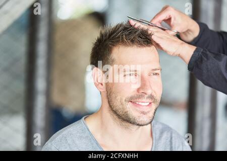 Mann bekommt einen Haarschnitt mit Schere beim Friseur oder Zu Hause Stockfoto