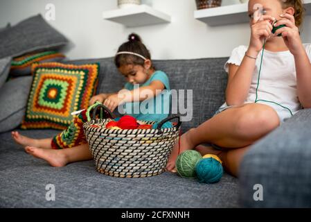 Kinder lernen zu stricken, sitzen auf der Couch im Haus. Mädchen Strick Häkeln. Selektiver Fokus auf Korb mit Garn und Hände von Kleinkind Mädchen. Stockfoto