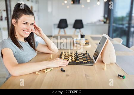 Lächelnde junge Frau spielt Schach in Video-Chat online bei Zu Hause auf einem Tablet-Computer Stockfoto