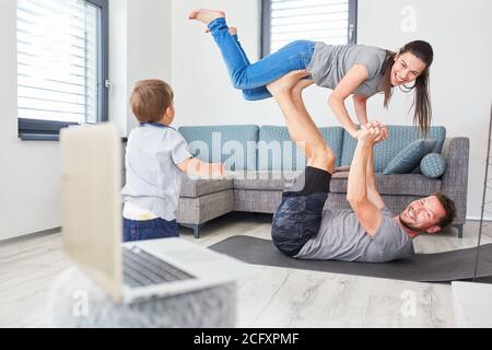 Eltern machen Gymnastik im Wohnzimmer mit Kleinkind und Laptop Computer im Vordergrund Stockfoto