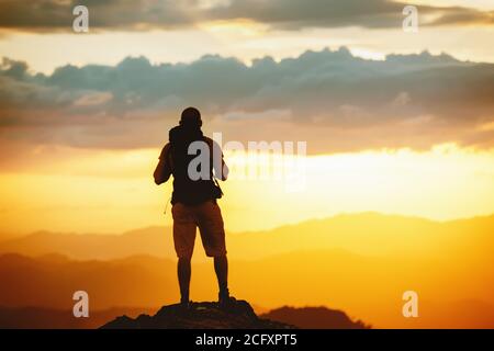 Unerkannte Wanderer steht mit Rucksack auf Berggipfel und genießt Sonnenuntergang am Himmel Stockfoto