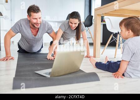 Eltern tun Liegestütze vor dem Laptop-Computer als Ein Video-Streaming-Fitnesskurs Stockfoto