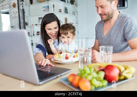 Familie mit Kind gratuliert zum Geburtstag im Video-Chat Mit hausgemachtem Kuchen Stockfoto