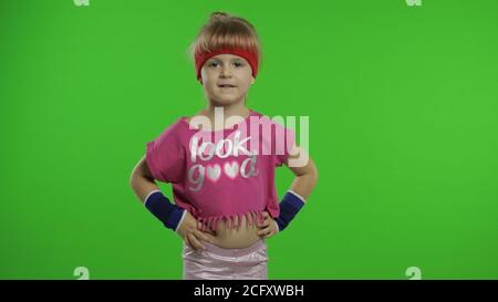 Kleine kaukasische Mädchen in rosa Sportanzug machen Fitness-Turner zu Hause Übungen. Workout für Kinder. Junge sportliche Kind in Sportbekleidung macht Warm-up, Stretching auf grünem Bildschirm, Chroma-Taste Hintergrund Stockfoto