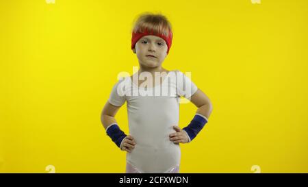 Kleine niedliche kaukasische Mädchen in weißen Sportbekleidung macht Fitness-Turner zu Hause Übungen. Workout für Kinder. Junge sportliche Kind im Sportanzug macht Warm-up, Stretching. Isoliert allein auf gelbem Hintergrund Stockfoto