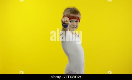 Kleine niedliche kaukasische Mädchen in weißen Sportbekleidung macht Fitness-Turner zu Hause Übungen. Workout für Kinder. Junge sportliche Kind im Sportanzug macht Warm-up, Stretching. Isoliert allein auf gelbem Hintergrund Stockfoto