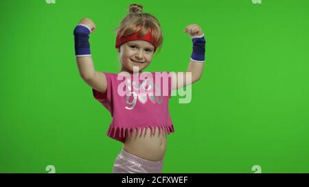 Kleine kaukasische Mädchen in rosa Sportbekleidung macht Fitness-Turner zu Hause Übungen, zeigt Muskeln. Workout für Kinder. Junge sportliche Kind in Sportanzug Trainingsbox, zeigt Faust Kampf. Chroma-Taste Stockfoto