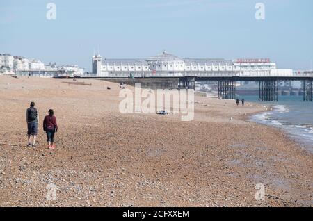 Ein paar Leute sitzen und gehen entlang eines leeren Brighton Beach während der Covid-19, Corona Virus Sperre, wo die Polizei ein Verbot von Strandbesuche erzwungen. Stockfoto