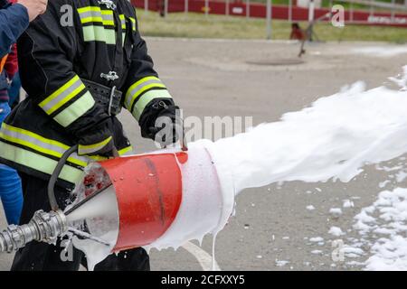 Lieferung von Schaum aus dem Schaumgenerator, Feuerlöschschaum fliegt aus dem Schaumgenerator, der den Feuerwehrmann in Kampfkleidung hält Stockfoto