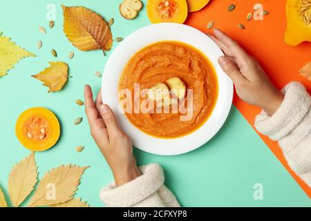 Frauenhände halten einen Teller mit Kürbissuppe auf einem zweifarbigen Hintergrund, eine stilvolle gesunde Mahlzeit Stockfoto