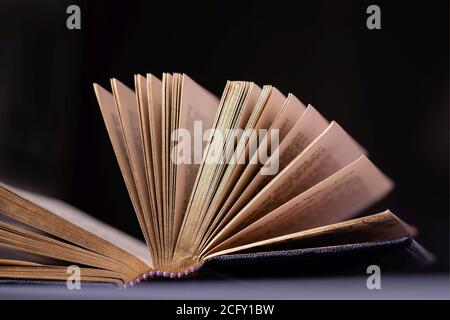 Geöffnetes altes Buch mit goldenen Seiten auf schwarzem Hintergrund Stockfoto