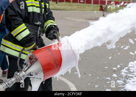 Lieferung von Schaum aus dem Schaumgenerator, Feuerlöschschaum fliegt aus dem Schaumgenerator, der den Feuerwehrmann in Kampfkleidung hält Stockfoto