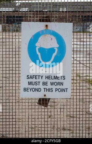 Schild am Zaun auf der Baustelle mit der Aufschrift: Sicherheitshelme müssen über diesen Punkt hinaus getragen werden Stockfoto