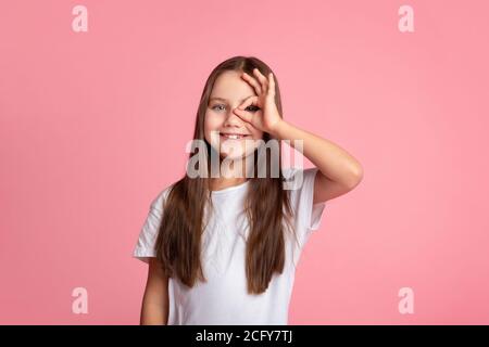 Alles ist cool. Lächelndes Kind tut ok Zeichen mit Hand auf Auge durch die Finger schauen Stockfoto