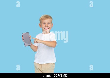 Niedliche smilling Kind Junge mit Smartphone auf blauem Hintergrund. Werbung für pädagogische Anwendungen auf einem Handy für Kinder. Lustiges Gesicht. Stockfoto