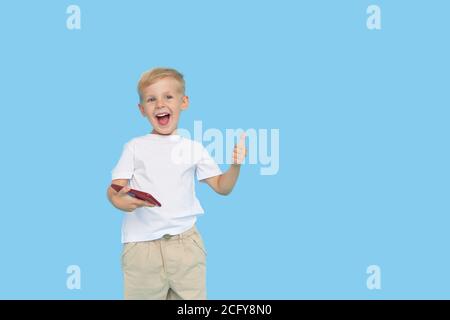 Niedliche smilling Kind Junge mit Smartphone auf blauem Hintergrund. Werbung für pädagogische Anwendungen auf einem Handy für Kinder. Lustiges Gesicht. Stockfoto