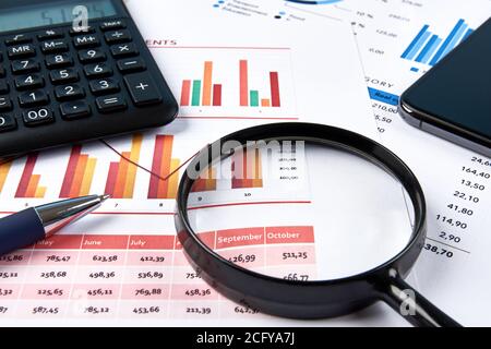 Ansicht des Büroarbeitsplatzes mit Finanzkarten und Zahlen, mit Taschenrechner, Lupe und Mobiltelefon. Blauer Stift auf weißem Papier. Stockfoto
