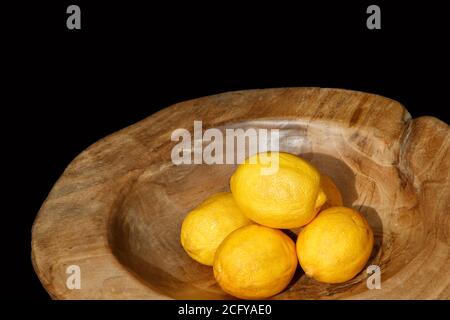 Gelbe Zitronen in einer runden Holzschale mit dunklem Hintergrund. Stockfoto
