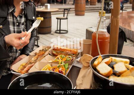Meeresfrüchte in Papierkartons auf dem Tisch und die Hand der Frau, die Essen nimmt. Street Food Stockfoto