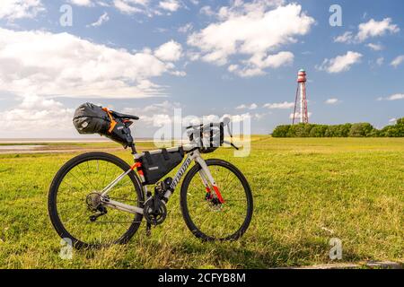 bikepacking an der Nordsee, Blick auf den Leuchtturm von campen bei emden mit einem gepackten Schotterrad vor der Nordsee, deutschland Stockfoto