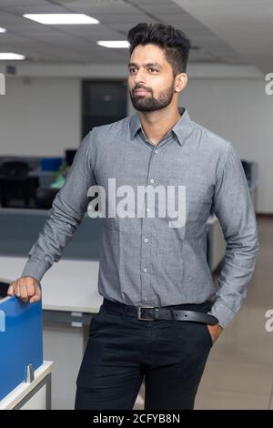 Porträt eines gutaussehenden jungen indischen Geschäftsmann lässig weg von der Kamera. Unternehmensumgebung. Stockfoto