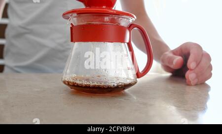 V60, Pourover. Hausgemachter Kaffee. Nahaufnahme von tropfendem Kaffee in einen Glasserver für die Herstellung eines Pourovers. Mann Braut zu Hause V60 Stockfoto